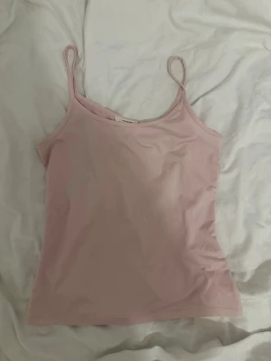 Ljusrosa linnetopp med smala band - Söt ljusrosa linnetopp med tunna axelband och enkel design. Perfekt att matcha med jeans eller kjol för en avslappnad look. Mjuk och skön känsla, passar till många olika stilar.