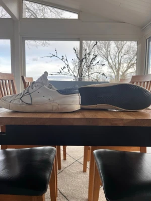 Vita sneakers från Philippe Model - Säljer ett par vita låga sneakers från Philippe Model med grå detaljer och den ikoniska loggan i blått på sidan. Skorna har en klassisk siluett, vit sula och är tillverkade i läder med textilfoder. Perfekta för en avslappnad och trendig stil. Skriv om ni vill ha fler bilder