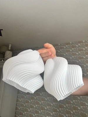 Vita snurriga lampskärmar 2 st  - Två vita lampskärmar i modern, vågig design. Tillverkade i plast med fin struktur som ger ett unikt och stilrent utseende. Perfekta för att skapa en cool belysningseffekt i rummet. Fästes enkelt med E14 sockel (tex ikea stråla för 49kr) 