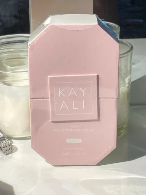 Kayali Yum Eau de Parfum 100ml - Kayali Yum Eau de Parfum i en snygg, ljusrosa flaska med vit geometrisk kork. Doften heter 'Yum Boujee Marshmallow | 81' och flaskan rymmer 100 ml. Förpackningen är också ljusrosa och har en modern, stilren design.