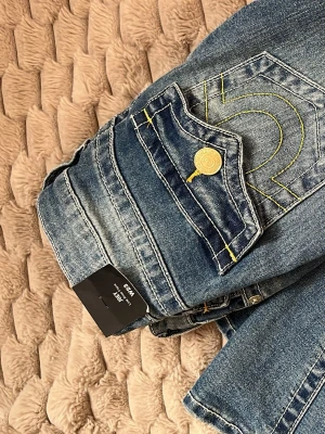 Blå True Religion jeans med gult mönster - Säljer ett par blå jeans från True Religion. Helt oanvända endast testade en gång! Med prislapp på, köpte för 1200kr