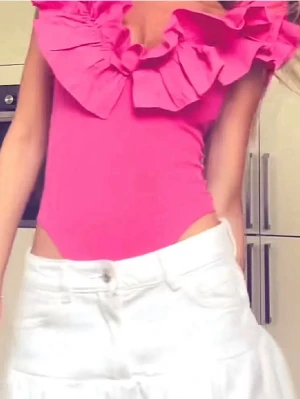 Rosa body med volangdetaljer - Trendig rosa body med volangdetalje. Tight passform. Perfekt för dig som vill sticka ut med en färgstark. Materialet är stretchigt och bekvämt.