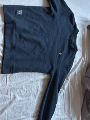 Mörkblå sweatshirt från Morris - Klassisk svart sweatshirt från Morris med rund halsringning och ribbade muddar. Liten Morris-logga broderad på bröstet och en patch nertill vid fållen. Perfekt basplagg i mjukt material som funkar året runt.