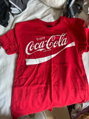 Röd Coca-Cola t-shirt XS - Snygg röd t-shirt från Coca-Cola med klassiskt vitt tryck framtill. T-shirten har rund hals och korta ärmar, perfekt för dig som gillar retrostil och vill sticka ut. Tillverkad i mjuk bomull för skön känsla hela dagen.