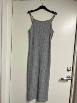 Grå ribbad långklänning - Snygg grå ribbad långklänning med smala axelband och rak passform. Klänningen har en enkel och stilren design som passar perfekt till sommaren. Tillverkad i mjukt och stretchigt material för extra komfort.