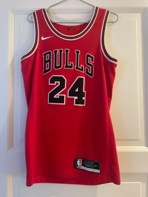 Chicago Bulls basketlinne Nike röd - Snyggt rött Chicago Bulls basketlinne från Nike med nummer 24 och namnet Markkanen på ryggen. Linnet har vita och svarta detaljer runt hals och ärmhål samt stor BULLS-text framtill. Perfekt för basket eller streetwear.