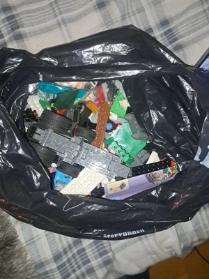Stor påse med blandade legobitar - En stor svart plastpåse fylld med blandade legobitar i olika färger och former. Innehåller bland annat hjul, plattor, byggklossar och specialdelar. Perfekt för dig som vill bygga egna kreationer eller fylla på din samling.