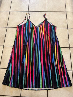 Färgglad randig sommarklänning storlek XL - Säljer en färgglad kortklänning med tunna axelband och v-ringning. Klänningen har ett randigt mönster i svart, blått, rosa, gult, grönt och rött. Perfekt för dig som vill sticka ut med en unik och lekfull stil under sommaren.