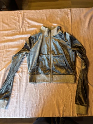 Grå velour hoodie med dragkedja - Snygg grå hoodie i mjuk velour med dragkedja framtill och två stora fickor. Tröjan har ribbade muddar vid ärmslut och nederkant samt hög krage. Perfekt för en avslappnad och trendig look.