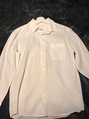 Vit linneskjorta från Uniqlo - Klassisk vit skjorta från Uniqlo i luftigt linne. Skjortan har lång ärm, bröstficka och knappar framtill. Perfekt för en clean och stilren look, lätt att matcha med olika outfits. Perfekt att använda nu när de börjar bli lite varmare väder! Fråga jättegärna mig om du har några du serif ar kring skjortan. Använda ett fåtal gånger!