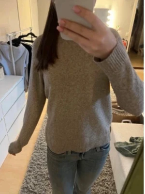 Beige stickad tröja i ullmix - Mysig beige stickad tröja med rund hals och långa ärmar. Tröjan har ribbade muddar vid ärmslut och nederkant, vilket ger en klassisk och enkel look. Perfekt för lager på lager under kyliga dagar.