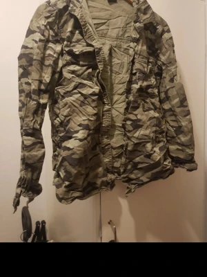 Klassisk camouflage skjorta - Camouflagefärgad skjorta med lång ärm och knappstängning framtill. Skjortan har flera fickor på bröstet och en avslappnad passform. Perfekt för dig som gillar militärinspirerad stil och vill sticka ut lite extra.