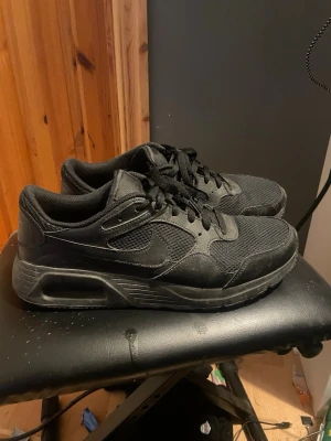 Svarta Nike Air Max sneakers - Snygga helsvarta Nike Air Max sneakers med klassisk siluett. Skorna har mesh och mockadetaljer, samt den ikoniska Air Max-sulan för extra komfort. Perfekta för dig som gillar en stilren och sportig look. Diskret Nike-logga på sidan och svarta skosnören. Dem är ca 2 månader gamla å har knappt använts därav säljer jag dem.