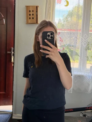 Mörkblå t-shirt från Lyle & Scott 12/13 år i storlek  - En klassisk mörkblå t-shirt från Lyle & Scott med deras ikoniska gula logga broderad på bröstet. T-shirten har rund hals och korta ärmar, tillverkad i mjuk bomull för en skön känsla. Perfekt till jeans eller shorts.