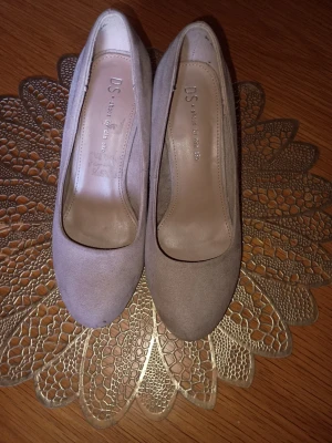 Beige pumps från DS Shoes - Snygga beige pumps från DS Shoes med rund tå och klädd klack. Skorna är i mockaimitation och har en stilren, klassisk design som passar till många olika outfits. Insidan är fodrad i ljust material för extra komfort.