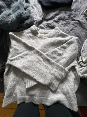 Ljusgrå stickad tröja Gina Tricot - Mysig ljusgrå stickad tröja från Gina Tricot med rund halsringning och ribbade muddar vid ärmslut och nederkant. Perfekt för lager-på-lager och enkel att matcha med jeans eller kjol. Tröjan har en klassisk, avslappnad passform och är tillverkad i mjukt material.