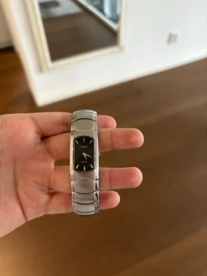Seiko silverfärgad rektangulär klocka - Säljer en vintage Seiko Vivace klocka med svart urtavla och silverfärgat metallarmband. Funkar som den ska men behöver bara nya batterier.