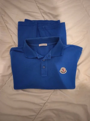 Blå Moncler piké med kort ärm - Snygg blå pikétröja från Moncler med klassisk krage och knappslå framtill. 100% äkta, storlek S true to size, känns som ny, mini svanker som inte syns se sista bild. Annars nyskick. 