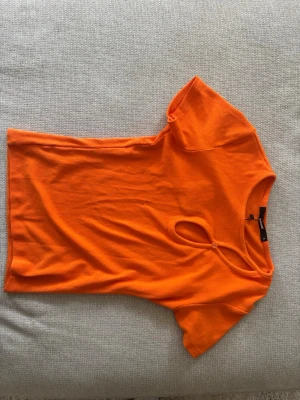 Orange ribbad topp från BikBok - Snygg orange ribbad topp från BikBok med korta ärmar och unik cut-out detalj vid halsen. Perfekt för dig som vill sticka ut med färg! Materialet är mjukt och stretchigt, vilket gör den bekväm att bära hela dagen.