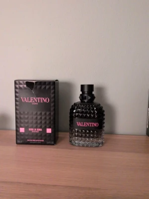 Valentino Uomo Born In Roma Intense - Valentino Uomo Born In Roma Intense är en lyxig parfym i en mörk, mönstrad glasflaska med svart och rosa detaljer. Flaskan har en unik nitar-liknande struktur och kommer med en matchande svart kartong med rosa text. Doften är intensiv och exklusiv. Ca 95/100ml kvar.