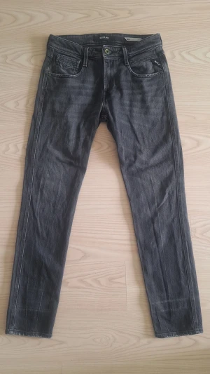 Grå slim fit jeans från Replay, anbass W30 L30 - Säljer ett par grå slim fit jeans från Replay, modell anbass, med klassisk femficksdesign och dragkedjegylf. Jeansen har en snygg tvättad look och raka ben. Materialet är mjukt denim som ger en skön känsla och passar perfekt till en avslappnad stil.