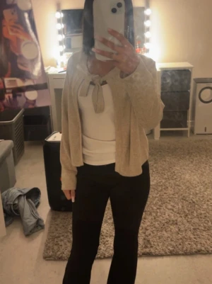 Beige kofta med knytning - Snygg beige kofta med knytning framtill. Koftan har en kortare modell och långa ärmar, perfekt att slänga över en topp. Mjuk och lättstickad, passar till många olika outfits.