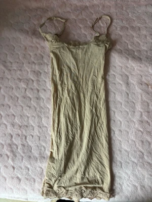 Beige nattlinne med spets från Skims - Säljer ett beige nattlinne från Skims i storlek XXS. Nattlinnet har tunna axelband och fina spetsdetaljer vid bysten och nederkanten. Tillverkat i mjuk polyamid och elastan för en skön känsla. Perfekt för mysiga kvällar hemma.