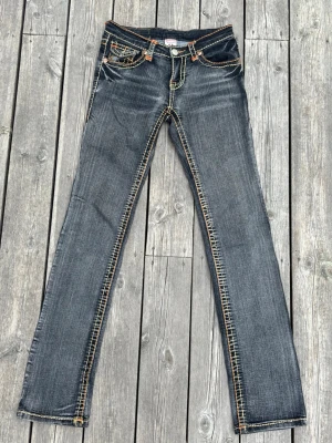 Vintage True Religion low rise jeans, mörkgrå - Mörkgrå Vintage jeans från True Religion med tydliga kontrastsömmar i orange och detaljer på bakfickorna. Klassisk femficksmodell i denim med låg midja och logopatch bak. Perfekta för dig som gillar street och en avslappnad look. Skriv privat om fler bilder/detaljer önskas