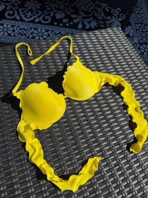 Gul glittrig bikiniöverdel från Calzedonia - Snygg gul glittrig bikiniöverdel från Calzedonia med volangdetaljer på banden. Bikinin har halterneck-knyt och knyts på ryggen💛💛 svårt med storlek men ungefär en C-kupa eller s/m