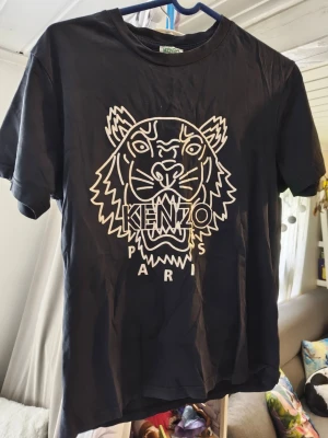Svart Kenzo t-shirt med tigertryck/S - Svart t-shirt från Kenzo med ikoniskt tigertryck och texten 'Kenzo Paris' på bröstet. Klassisk passform med rund hals och korta ärmar. Perfekt för dig som vill sticka ut med en stilren och trendig look. Kan inte garantera äkthet 