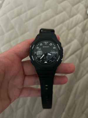 Svart digital sportklocka från Sanda - Cool svart digital sportklocka från Sanda med både analog och digital display. Klockan har flera funktioner som ljus, start/stop och mode-knappar. Armbandet är i syntetmaterial och designen är sportig och modern.