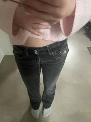 Svarta bootcut jeans med vita sömmar - Säljer ett par svarta bootcut jeans med vita kontrastsömmar och dubbla knappar i midjan. Jeansen har fickor fram och bak samt en lätt utsvängd passform nertill. Perfekta för dig som gillar en klassisk men trendig look.