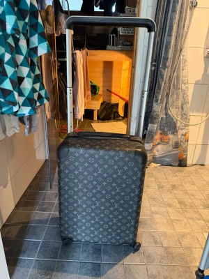 Louis Vuitton Black Horizon 55 Suitcase - Snygg grå resväska från Louis Vuitton med klassiskt monogrammönster i vitt. Väskan har hårt skal, fyra hjul och teleskophandtag. Utrustad med TSA-lås och dragkedja. Perfekt för dig som vill resa med stil.