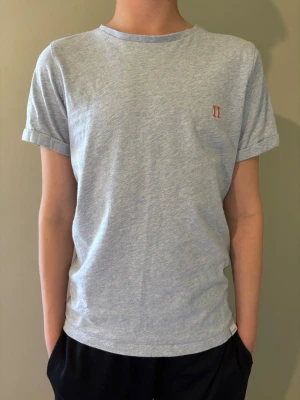 Ljusblå t-shirt från Les Deux - Snygg ljusblå t-shirt från Les Deux med liten broderad logga på bröstet. T-shirten har korta ärmar med uppvik och är gjord i mjuk bomull. Perfekt för en avslappnad och stilren look.