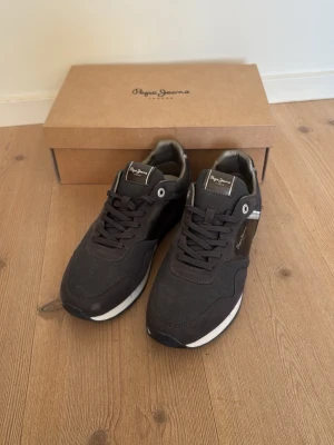 Grå trainers Pepe Jeans - Snygga sneakers från Pepe Jeans med vita detaljer på sulan och logga på sidan. Skorna har klassisk låg modell, snörning och ovandel i mockaliknande material. Perfekta för en stilren och avslappnad look. De är i nyskick endast använda ett fåtal gånger. Storleken är 41 men är lite liten i storleken så passar också 40.