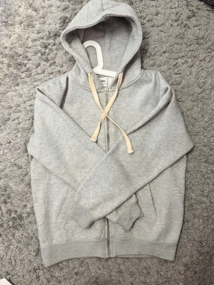Ljusgrå zip-hoodie med fickor - Ljusgrå hoodie med dragkedja från Zara. Klassisk modell med huva och beige dragsnören, samt två fickor framtill. Tillverkad i mjuk bomullsblandning, perfekt för en avslappnad stil.