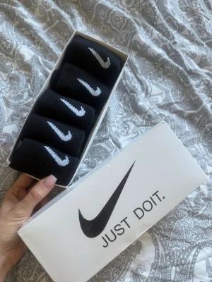 Svarta Nike strumpor i 5-pack - Säljer ett 5-pack svarta strumpor från Nike med klassisk vit swoosh-logga. Strumporna är ribbade och tillverkade i mjuk bomull, perfekta för en sportig och stilren look. Kommer i originalförpackning med Nike-tryck. Strl 36-39