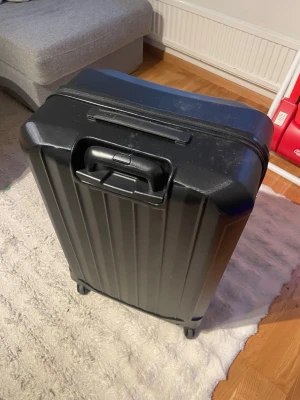 Svart hård resväska från Epic - Snygg svart resväska från Epic med hårt skal och fyra hjul för smidig transport. Väskan har ett stilrent räfflat mönster och teleskophandtag. Perfekt för dig som vill resa med stil och ha en tålig väska i klassisk design. Dragkedjan till innerfacket är trasigt men inget som påverkar funktionen på väskan 75x50x32