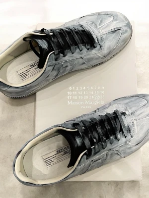 Maison Margiela - Maison Margiela sneakers i vitt med handmålad effekt och svarta skosnören. Lågt skaft, klassisk siluett och vit innersula. Tillverkade i läder med unik borstad finish som ger en cool, konstnärlig vibe. Dessa väldigt unika margeila har inte ”de flesta” vilket jag tycker gör de till en underbar sko ⭐️frågor? Tveka inte hör av dig 🤙 andvända ett fåtal gånger 