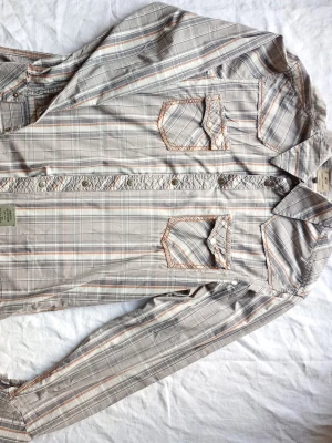 Beige rutig skjorta med fickor - Snygg beige rutig skjorta från Jack & Jones med långa ärmar och två bröstfickor med knappdetaljer. Skjortan har klassisk krage och knäppning framtill. Perfekt för en avslappnad men stilsäker look.