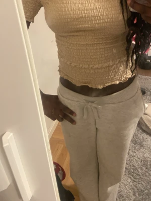 Beige croppad smockad topp - Säljer en beige croppad topp med smockad struktur och volangkant nedtill. Toppen är kortärmad och har en tajt passform som framhäver midjan. Perfekt att styla med höga byxor eller kjol. Materialet känns som bomull eller polyester.