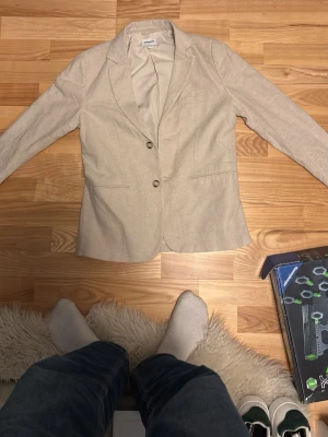 Beige kavaj från Kappahl - Stilren beige kavaj från Kappahl i storlek 164. Kavajen har två knappar framtill, klassisk krage och två fickor. Materialet känns mjukt och har en lätt struktur, perfekt för ett finare ställe. Är öppen för förhandling 