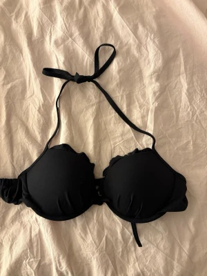 Svart bikiniöverdel med volang - Snygg svart bikiniöverdel med volangkant runt kuporna och knyt i nacken. Använd enstaka gång