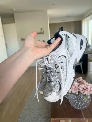 Vita New Balance 530 sneakers - Snygga vita New Balance 530 sneakers med mesh och syntetdetaljer. Skorna har marinblå inslag, klassisk N-logga på sidan och bekväm sula med ABZORB-dämpning. Perfekta för en sportig och trendig look.