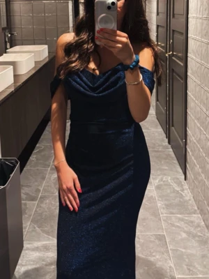 Marinblå glittrig balklänning - Säljer en marinblå balklänning med glittrigt tyg och offshoulder-design. Klänningen har en draperad urringning och smickrande passform som framhäver figuren.  Endast använd under 2 tillfällen💙💃🏽