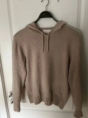 Beige cashmere hoodie från Sayless - Mysig beige hoodie från Sayless i mjuk cashmere. Klassisk modell med huva och dragsko, ribbade muddar vid ärmslut och nederkant. Perfekt för dig som gillar stilrena och bekväma plagg med exklusiv känsla.