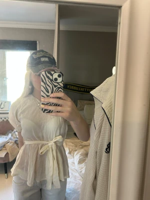 Vit omlottopp med knytband - Säljer en luftig vit omlottopp med ett brett knytband i midjan. Toppen har en lätt rynkad struktur, kort ärm och en avslappnad passform. Perfekt för varma dagar och enkel att styla med smycken eller jeans.