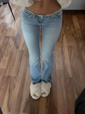 Ljusblå bootcut jeans låg midja - Säljer ett par ljusblå bootcut jeans med låg midja och klassisk femficksdesign. Jeansen har en lätt utsvängd passform nedtill och är perfekta för en avslappnad och trendig look. Materialet är mjukt denim i bomull med lite stretch.