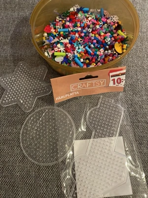 Pärlplattor och pärlor i mixade färger - Säljer ett set med genomskinliga pärlplattor i olika former och en burk med massor av färgglada plastpärlor. Perfekt för kreativa pysselstunder och att skapa egna mönster. Plattorna är i former som stjärna, cirkel och julkula.