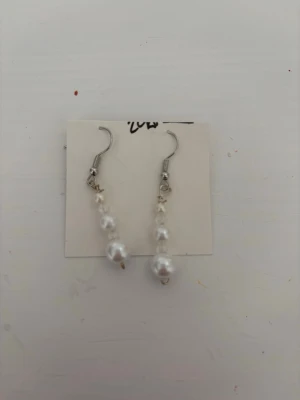 Silvriga örhängen med vita pärlor - Säljer ett par snygga hängande örhängen med två vita pärlor på varje örhänge. Krokarna är i silverfärg och designen är enkel men elegant. Perfekta för dig som gillar klassiska accessoarer med en modern touch.